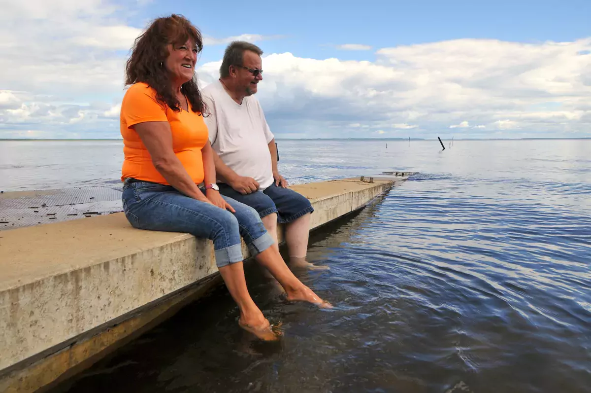 A couple sit on a dock in Plamondon Lac La Biche looking out at the water