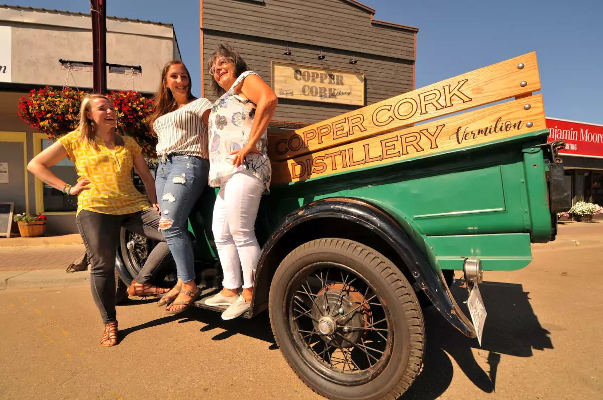 Three women stand in front of a 1928 Model A Ford Roadster Truck outside Copper Cork Distillery