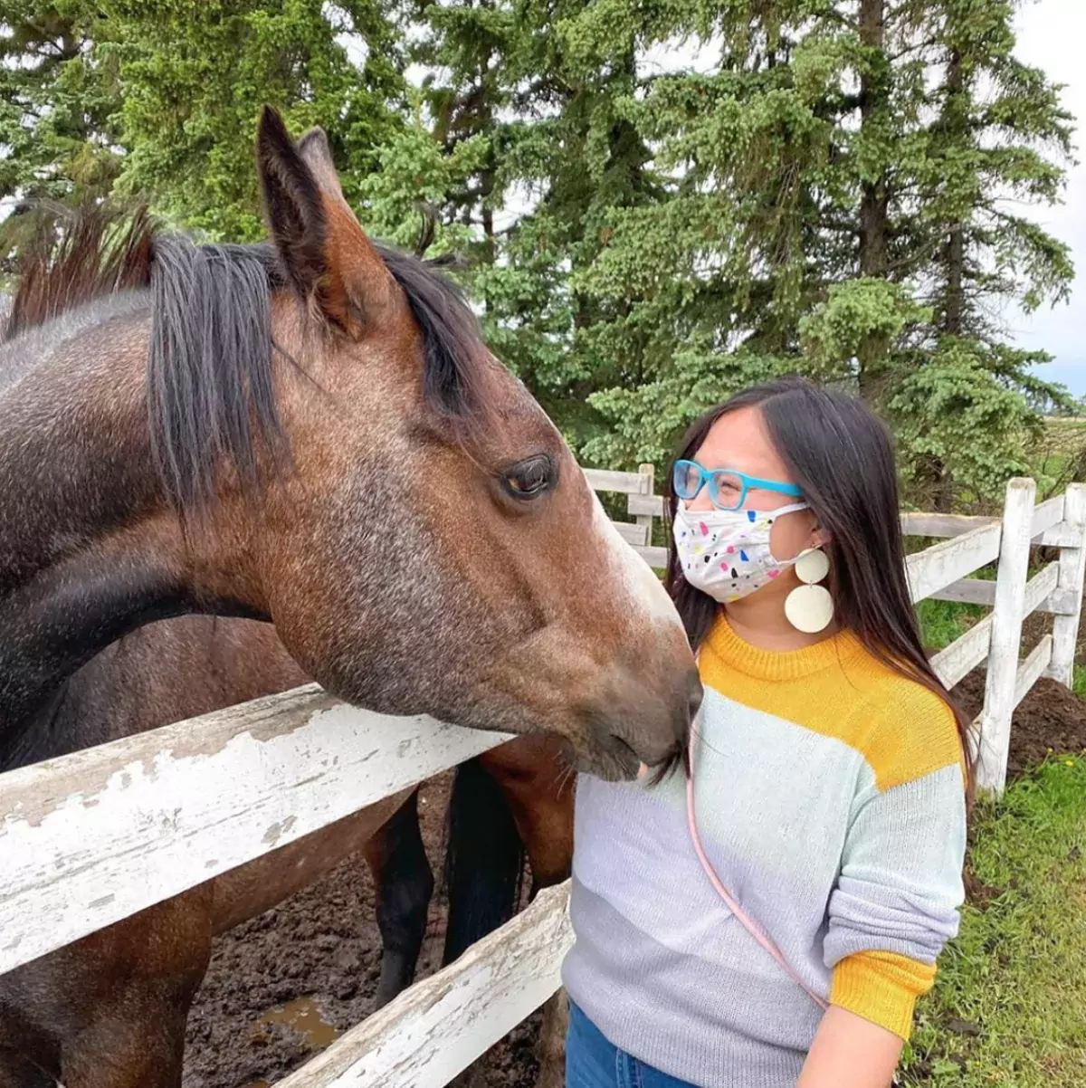 A woman pets a horse in a stable with a face mask on